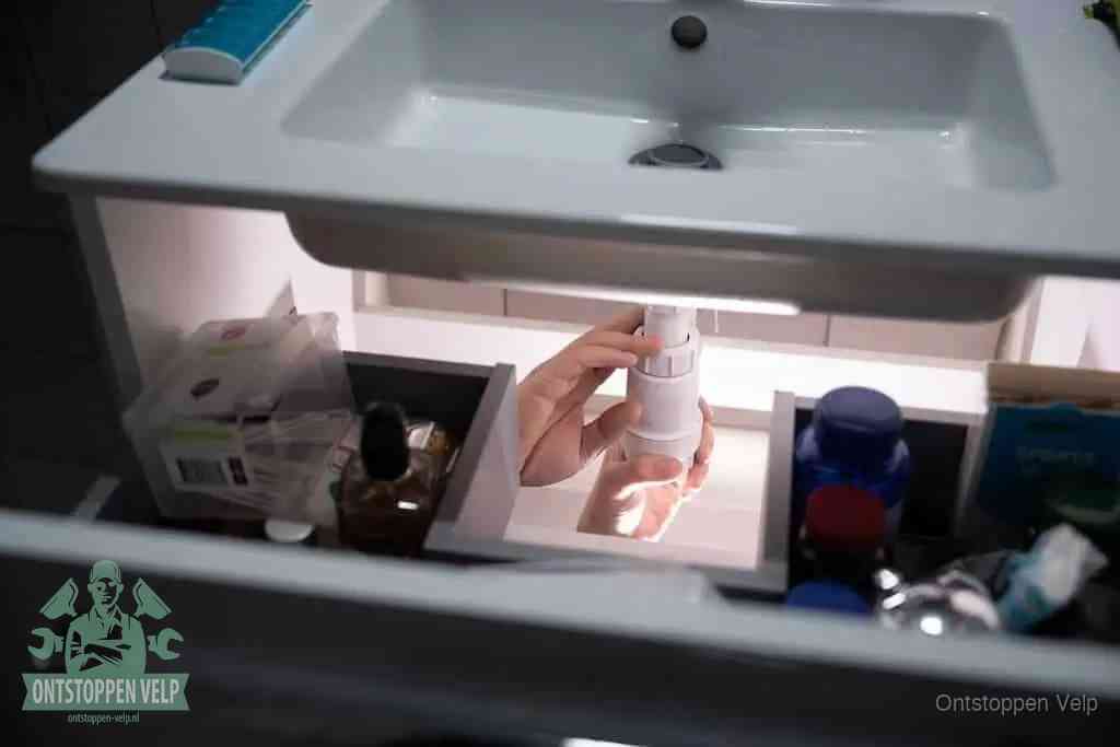 Een pompfles met zeep boven een wastafel, de heet water en afwasmiddel-methode om een vetprop in de afvoer los te maken in Velp
