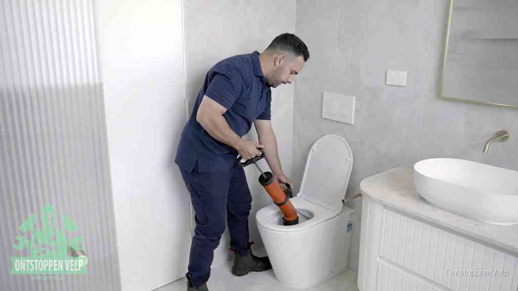 Een monteur buigt over een wandcloset en duwt met de hand een persluchtontstopper in de toiletpot om de verstopping handmatig los te maken in Velp