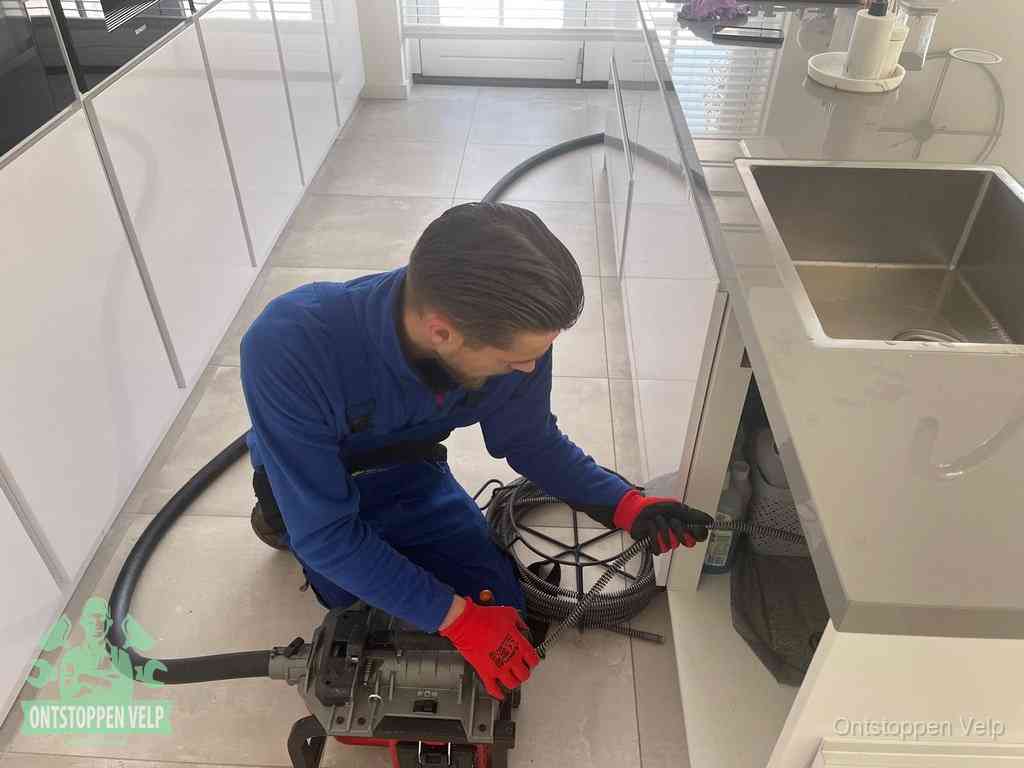 Een monteur ontstopt de keukenafvoer onder de spoelbak met een elektrische veermachine in Velp