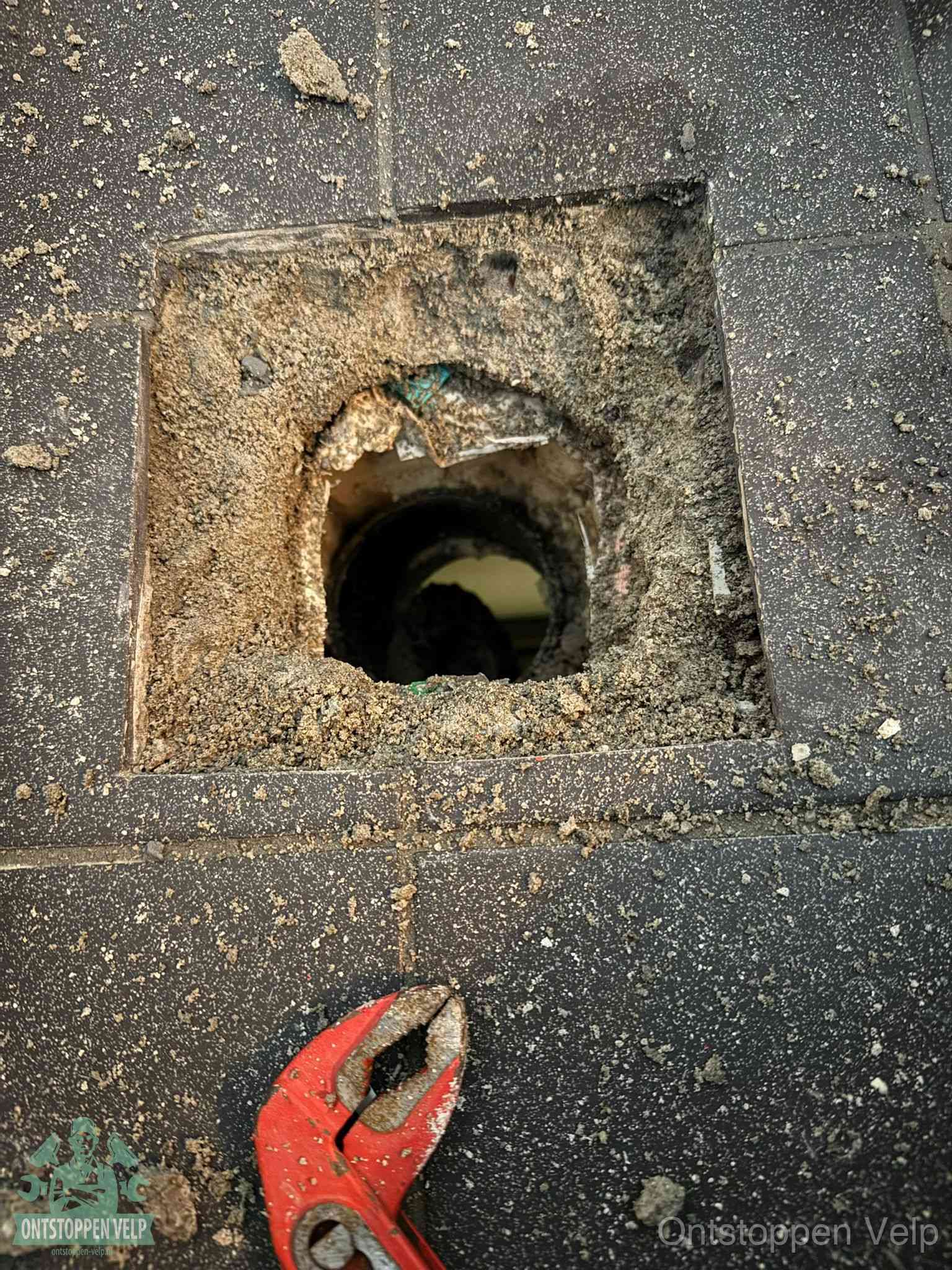 Een geopend rioolputje in een betontegelvloer met losgemaakt rooster en een zichtbare ronde afvoerbuis, het achterhalen waar de afvoerverstopping zit in Velp