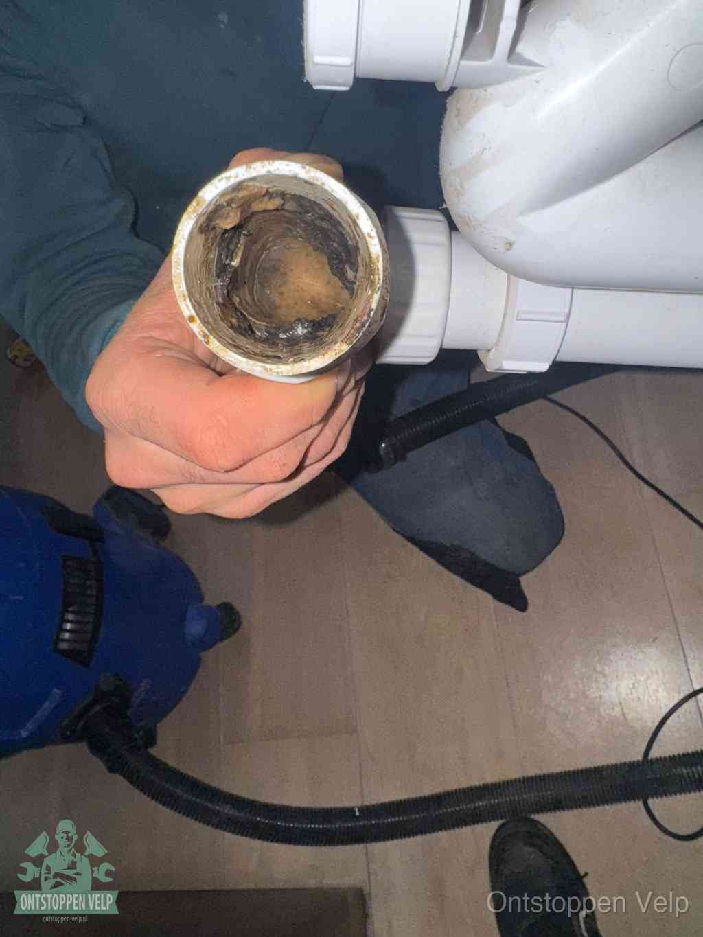 Een hand houdt een losgekoppeld PVC-afvoerbuisstuk vast dat van binnen volledig is dichtgeslibd met vet, vuil en aanslag, de meest voorkomende oorzaak van een verstopte afvoer in Velp
