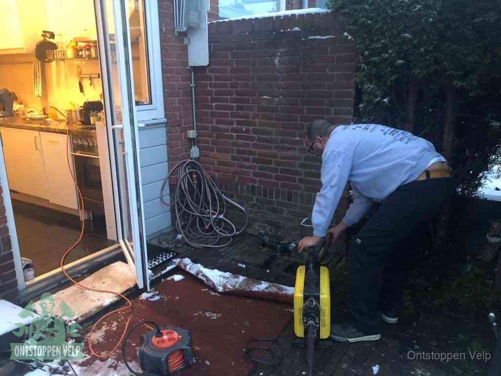 Een monteur werkt buiten bij een open riool-/grondput met een elektrische ontstoppingsmachine om een verborgen afvoerprobleem op te sporen in Velp