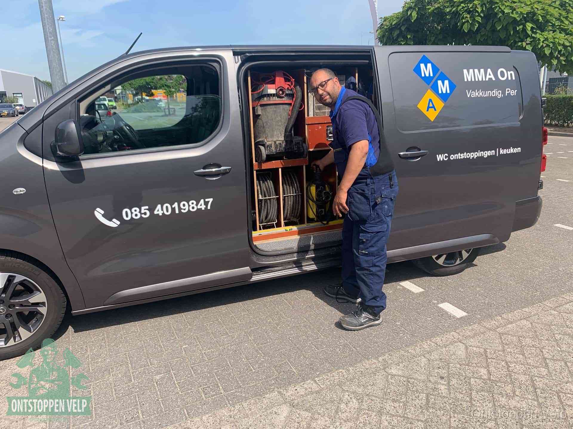 Een monteur bij de open schuifdeur van zijn bedrijfsbus op een parkeerplaats, klaar om de oorzaak van terugkerende afvoerverstoppingen aan te pakken in Velp