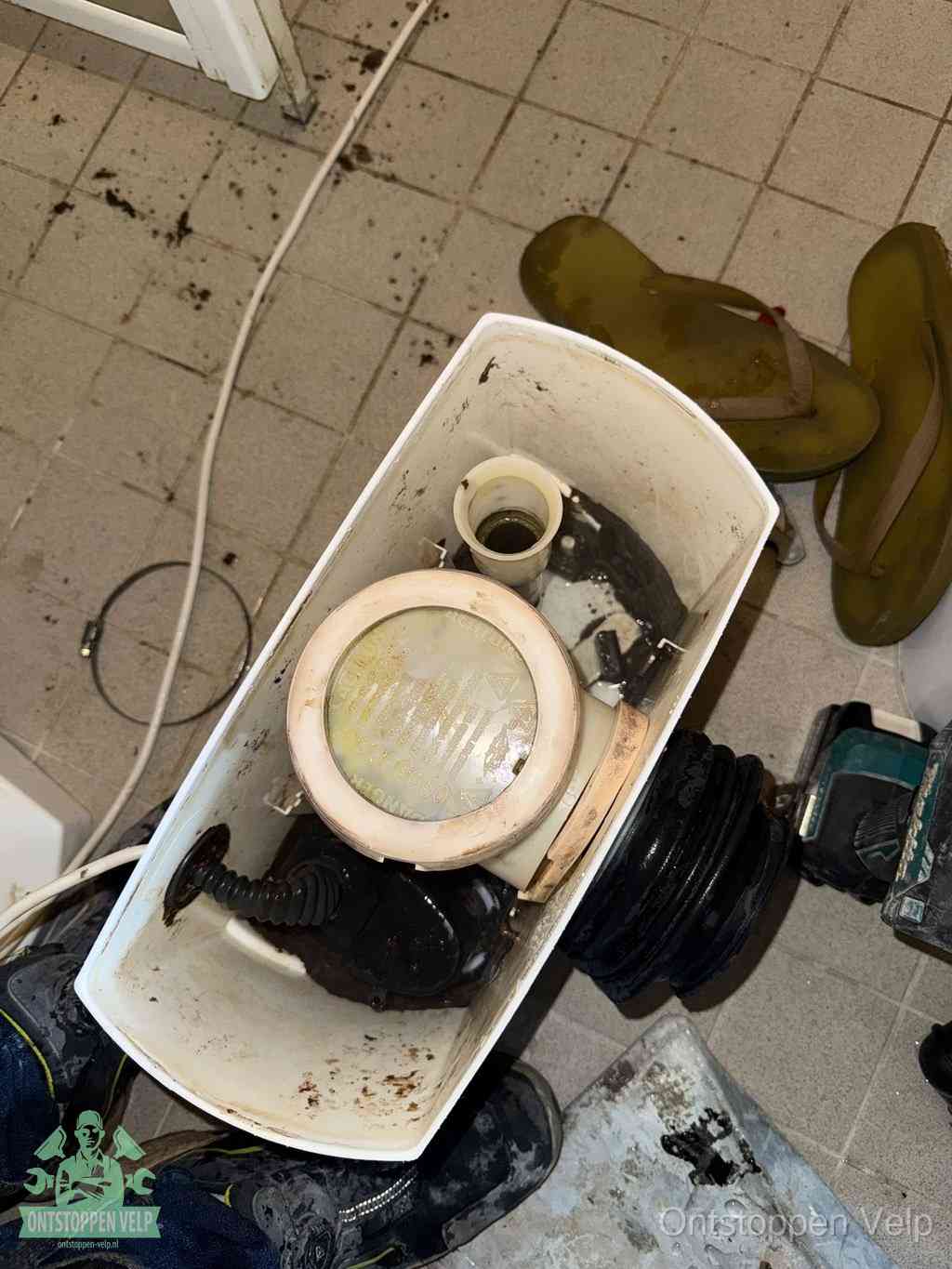Een gedemonteerde toiletpot op de vloer met ontstoppingsveer en gereedschap ernaast, het verwijderen van een vastzittend voorwerp uit de wc in Velp