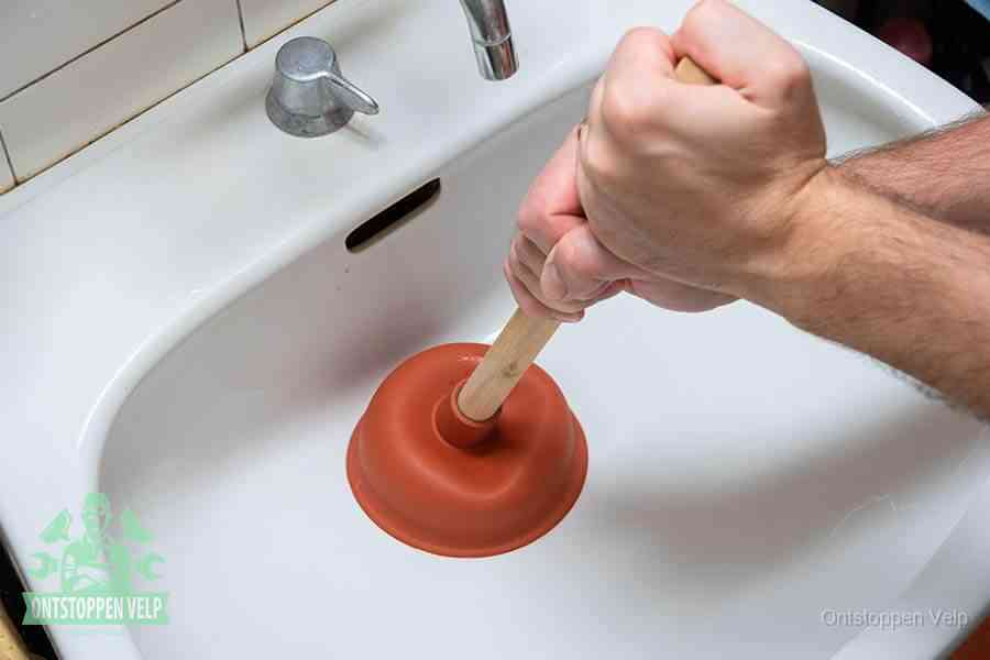 Twee handen gebruiken een rode rubberen plopper op een sanitair-afvoer om het toilet te ontstoppen in Velp