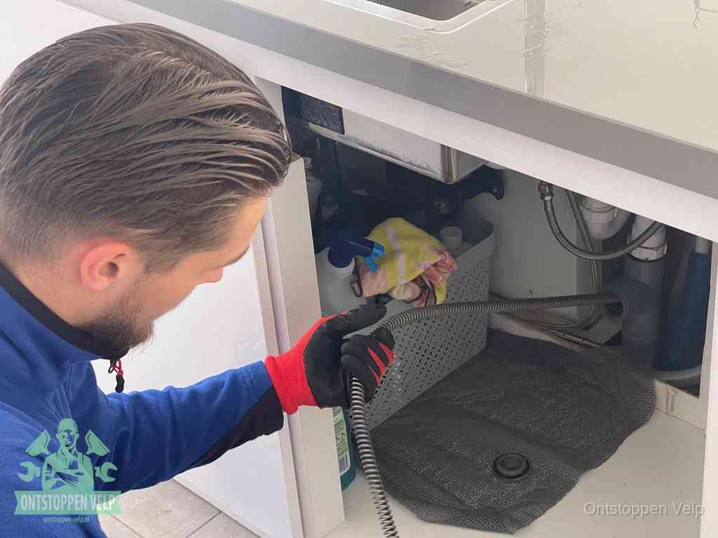 Een monteur voert een flexibele ontstoppingsveer in de afvoer om een verstopping voorbij de bocht van het toilet te bereiken in Velp