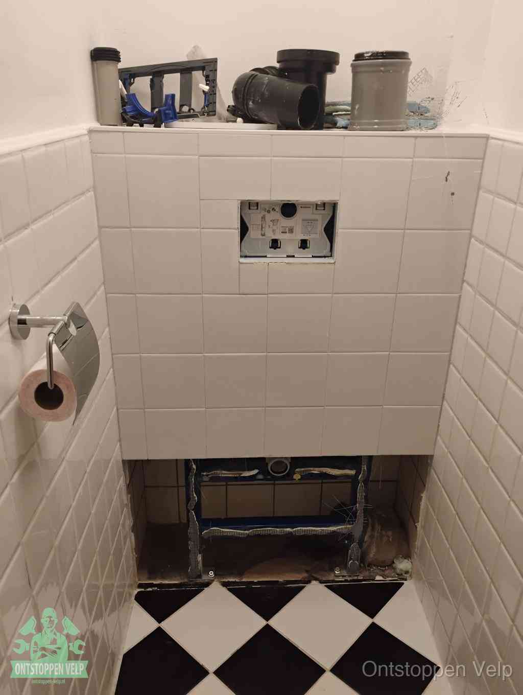 Een toiletruimte waar het hangtoilet en de inbouwreservoir-onderdelen zijn vrijgelegd voor onderhoud, periodiek nazicht voorkomt een wc-verstopping in Velp