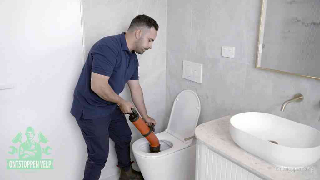 Een man gebruikt een handmatige luchtdruk-ontstopper in een modern betegeld toilet om zelf de wc te ontstoppen in Velp